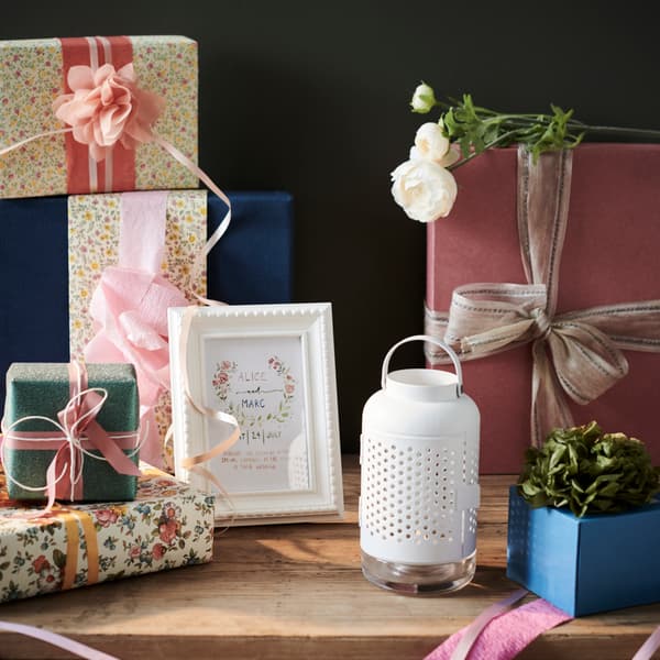Verschillende soorten ingepakte cadeaus op een houten tafel. In het midden staat een fotolijstje en daarnaast een witte lantaarn.