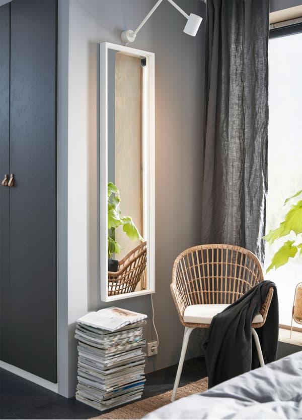 Vertikalno okačeno IKEA NISSEDAL belo ogledalo na zidu pored NILSOVE stolice s rukohvatima od ručno pletenog ratana i bambusa.