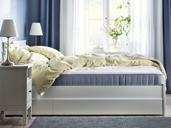 VESTERÖY hybrid mattress in brightly lit bedroom with blue curtains and white sheers