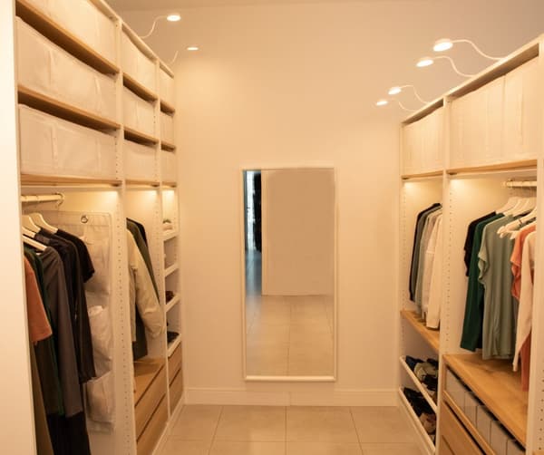 Vestidor blanc amb roba penjada en penjadors, espai d'emmagatzematge a la part superior amb caixes, calaixos, sabater i un mirall.