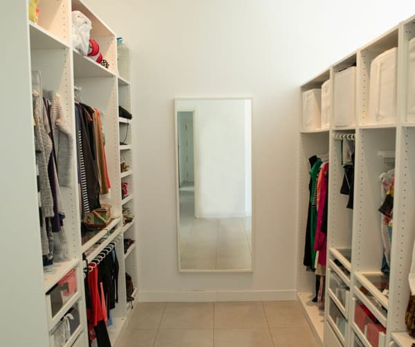 Vestidor blanco con ropa colgada en perchas, cajones y un espejo.