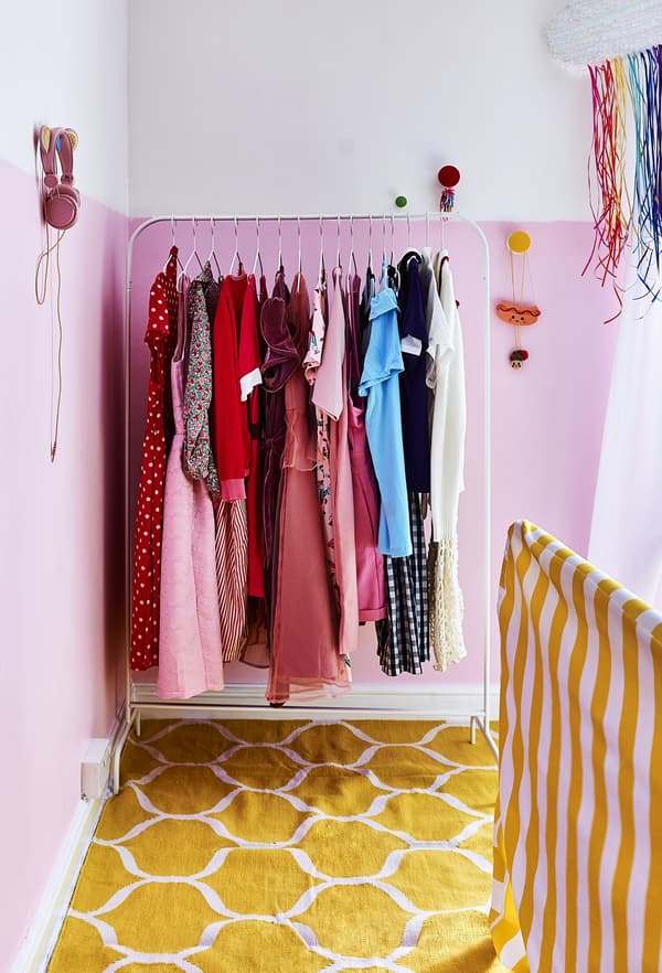 Vêtements colorés accrochés à une tringle dans une chambre rose.