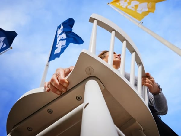 Вид снизу на человека, несущего деревянный стул, над которым развеваются яркие флаги IKEA.