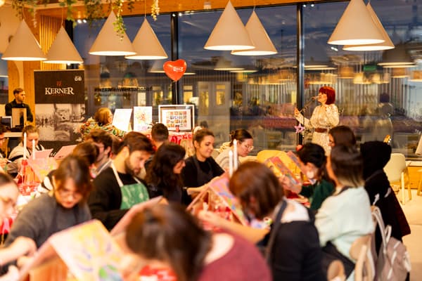 Viele Teilnehmer malen in einer IKEA-Restaurant-Atmosphäre, während eine Sängerin im Hintergrund auftritt.

