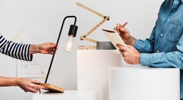 Vienas asmuo laiko lempos prototipą, kiti užsirašinėja pastabas