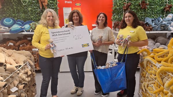 Vier Frauen, darunter zwei IKEA-Mitarbeiterinnen in gelben Shirts, halten einen Spendenscheck über 1'250 Euro für den Deutschen Kinderschutzbund. Sie stehen in der IKEA-Kuscheltierecke, umgeben von Stofftieren, und halten einige in den Händen.