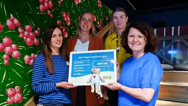 Vier Frauen stehen in einem farbenfrohen, kindgerecht gestalteten Raum und halten gemeinsam einen Spendenscheck über 3.500 Euro von IKEA Siegen für das GFO Haus, eine Mutter-Vater-Kind-Einrichtung. Zwei der Frauen tragen IKEA-Mitarbeiterkleidung, während die anderen Freizeitkleidung tragen.  