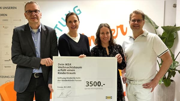 Vier Personen stehen in einem Innenraum und halten gemeinsam einen großen Spendenscheck über 3.500 Euro von IKEA Regensburg. Der Scheck ist für die Stiftung „Kinderlächeln“ der Kinderklinik Passau bestimmt. Im Hintergrund sind eine Wand mit Schriftzug und verschiedene Sponsorentafeln zu sehen.  