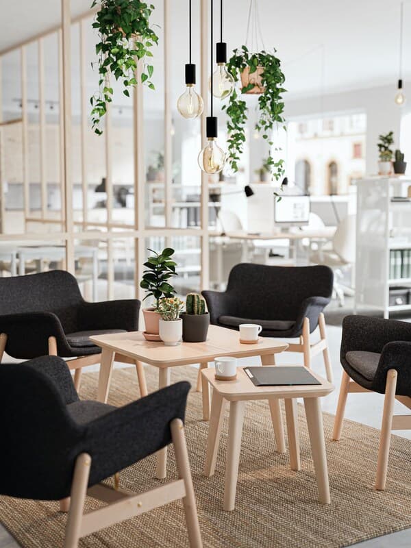 Vier schwarze Sessel und zwei Tische aus hellem Holz im Loungebereich eines Büros.