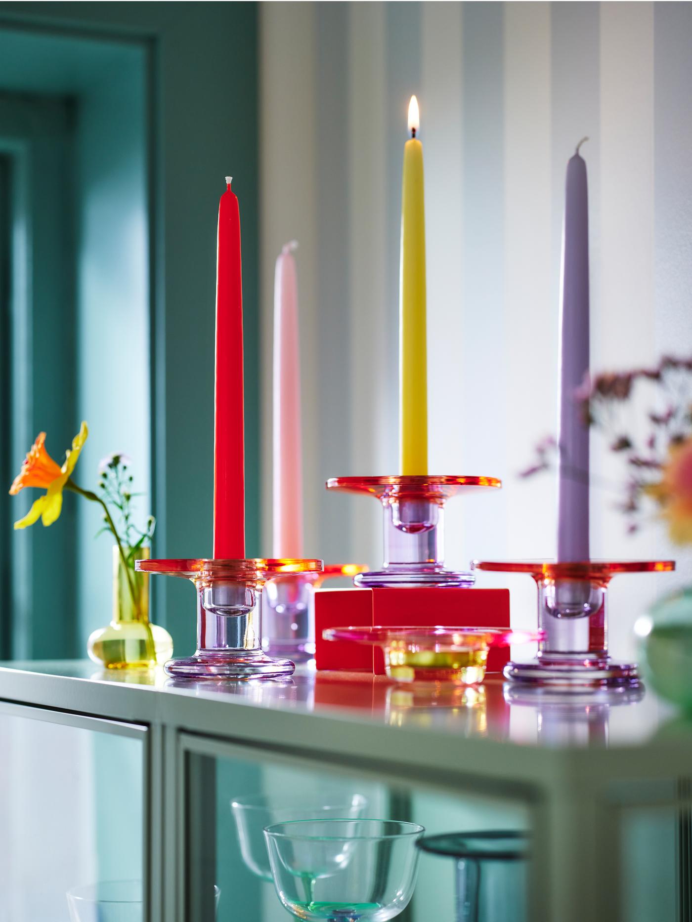 Vier TJÄRLEK Kerzenständer, ein TJÄRLEK Teelichthalter und eine TJÄRLEK Vase stehen auf einer Vitrine.