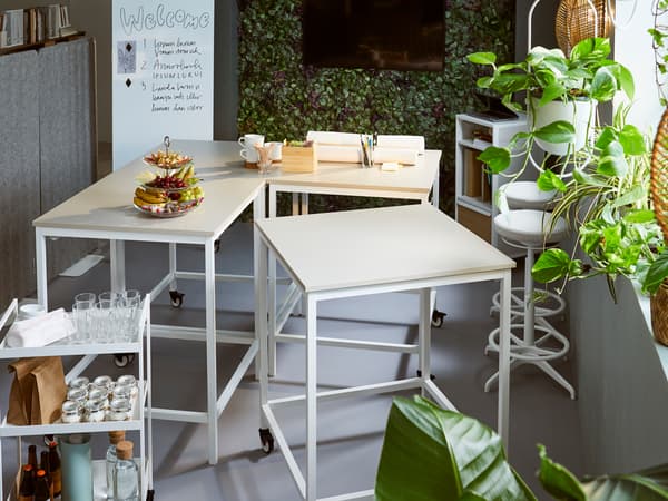 Vier TROTTEN tafels in beige/wit en een witte NISSAFORS roltafel staan in een kantoorruimte met enkele planten