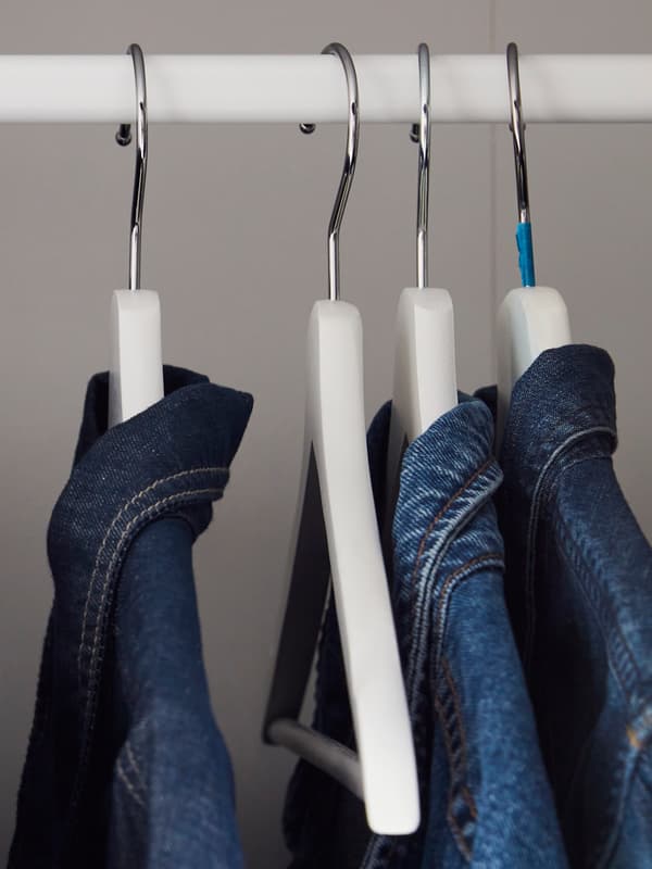 Vier witte kleerhangers hangen aan een metalen stang, elk met een blauwe jeans erover gedrapeerd, tegen een neutrale achtergrond.
