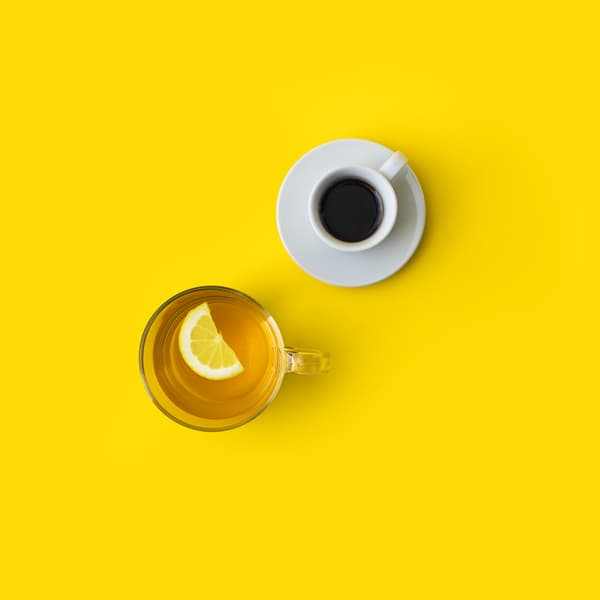 View from above of a mug of coffee and a mug of tea with lemon on a yellow background.