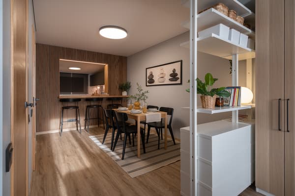 View into a contemporary dining area with a wooden table and black chairs, light wood floors, minimalist decor, and open shelving partially dividing the space.