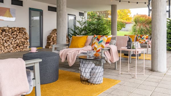 View of a large terrace with benches on which there are seat cushions, pillows and blankets
