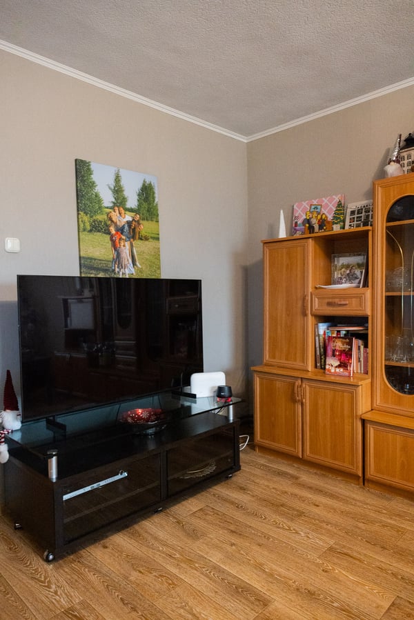 View of a living room corner with a large television and wooden cabinets on both sides. The room is functional but visually filled with furniture and belongings.