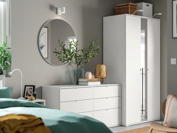 VIHALS wardrobe and chest of drawers combination in bedroom. A NISSEDAL round mirror is mounted on the wall above the drawers, and there are also storage boxes and a table lamp laced on top.  