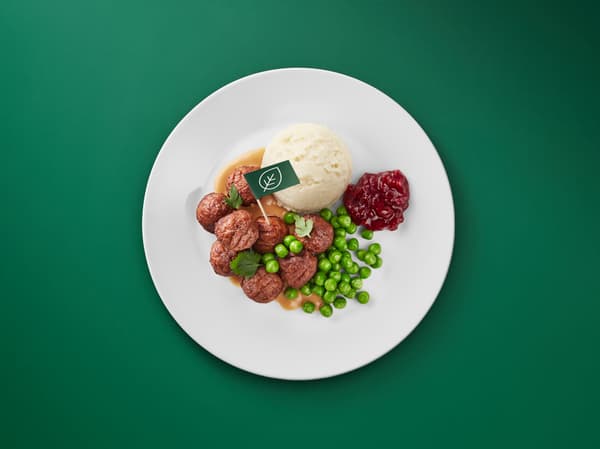 Vihreää taustaa vasten pyörykkäannos, jossa kasviproteiinipyöryköitä, perunamuusia, herneitä ja puolukkahilloa.