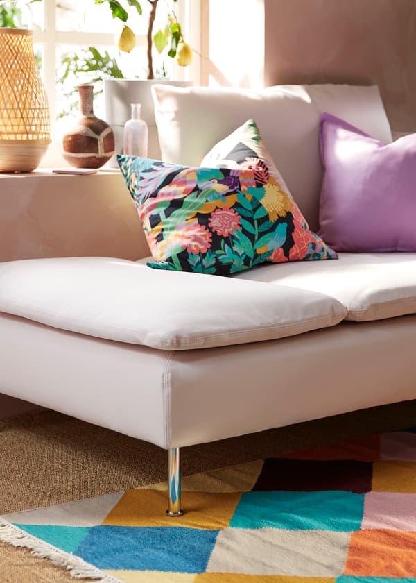 Világos színvilágú kanapé, színes párnákkal és vidám, tarka szőnyeg.