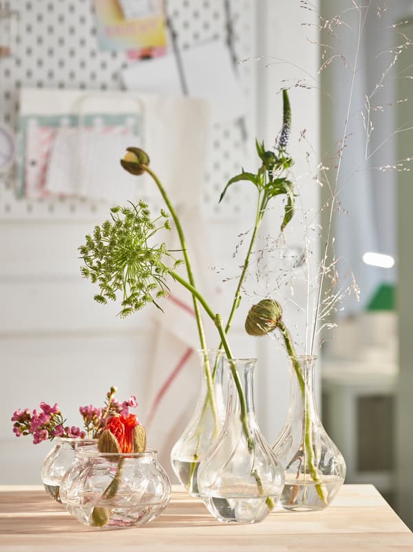 VILJESTARK glasvaser i forskellige højder med en enkelt eller nogle få blomster står på et rullebord af træ i køkkenet.