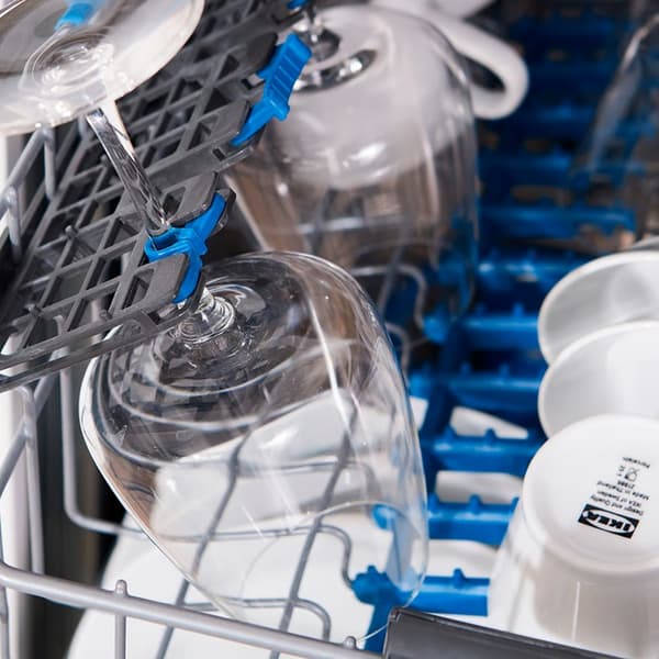 Vīna glāzes nostiprinātas trauku mazgājamās mašīnas augšējā plauktā kopā ar baltām krūzēm.