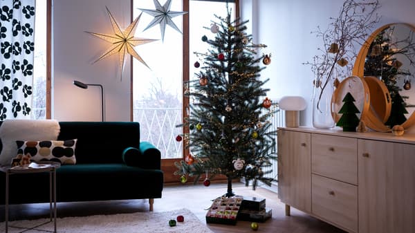 VINTER 2021 holiday tree is decorated with ornaments in a living room setting beside a green sofa and hanging stars.