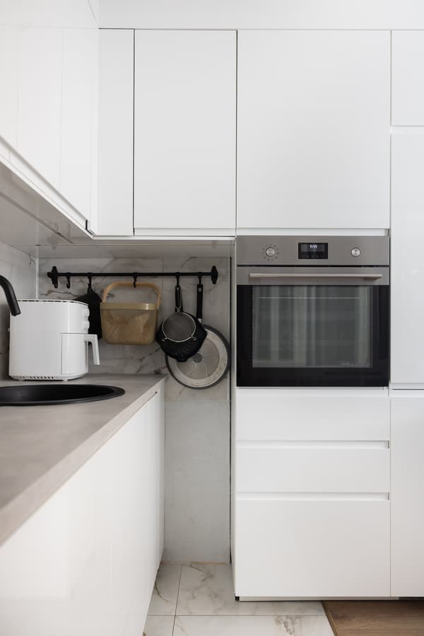 Virtuves stūris ar augstajiem skapjiem un iebūvētu cepeškrāsni; redzami slēgti skapīši un sakārtota darba virsma.