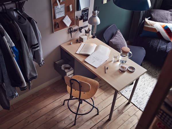 Vista angular del dormitorio donde se ve un escritorio y una silla delante, y un diván de fondo.