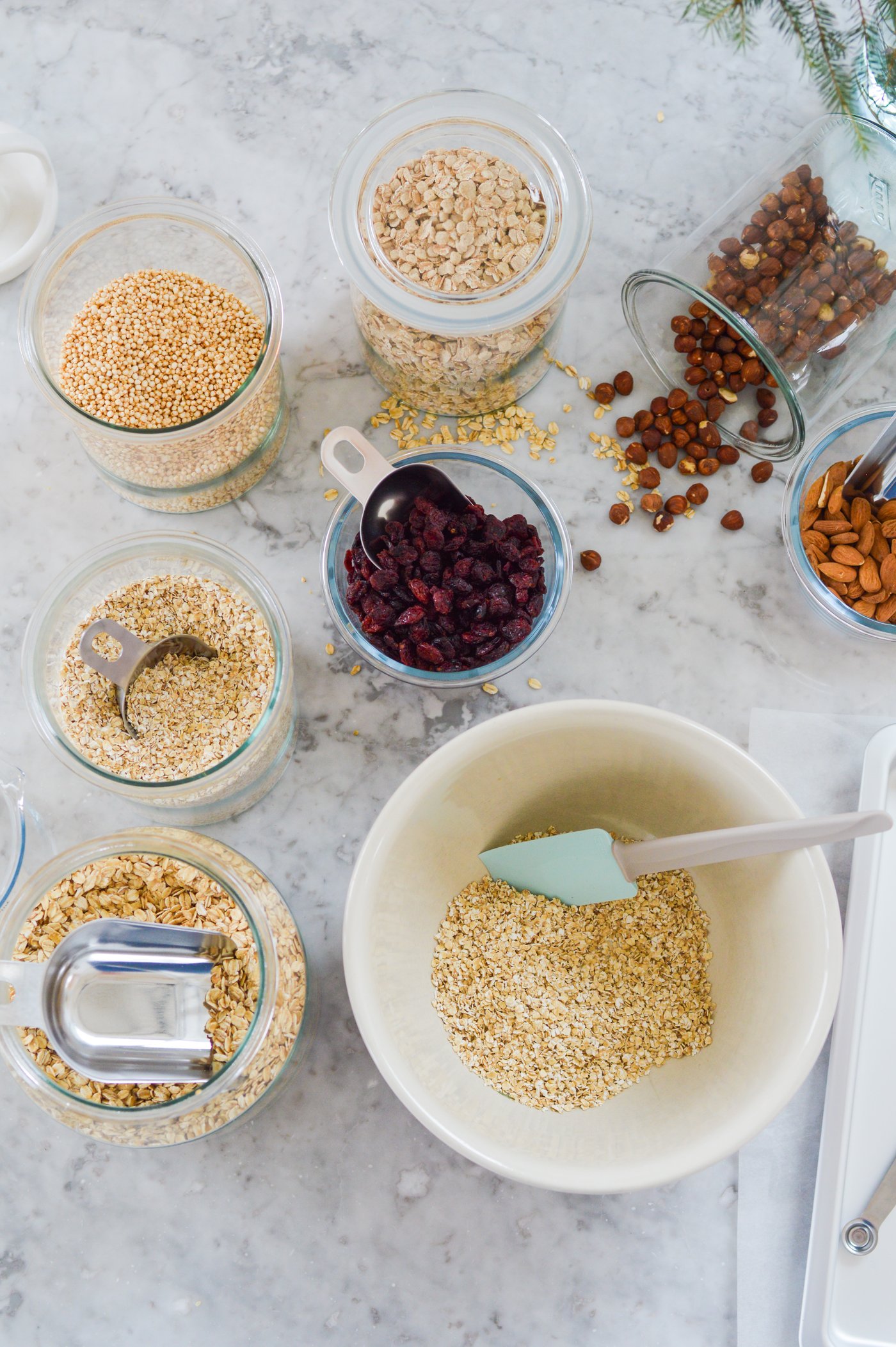 Vista dall'alto di diversi tipi di cereali, noci e bacche essiccate in ciotole e barattoli di vetro su una superficie di marmo. Al centro c'è una ciotola con cereali e una spatola.
