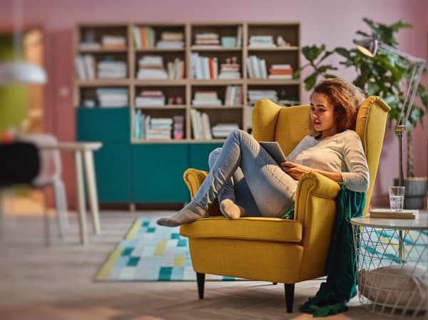 Vista frontal de un living con un sofá amarillo de la serie STRANDMON con una persona sobre el leyendo una revista.
