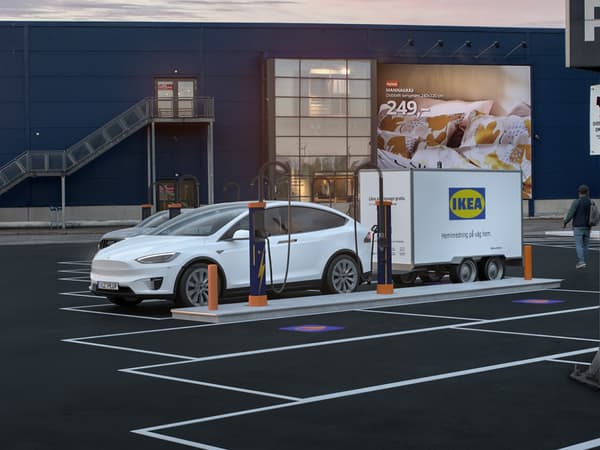 Vit elbil med släpvagn från IKEA står vid laddstation utanför ett varuhus