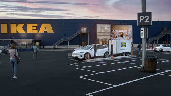 Vit elbil med släpvan från IKEA står vid laddstation utanför ett varuhus