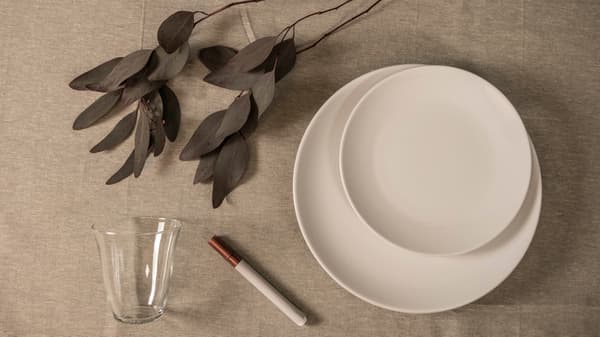 Vita tallrikar, glas och porslinspenna på en duk. 