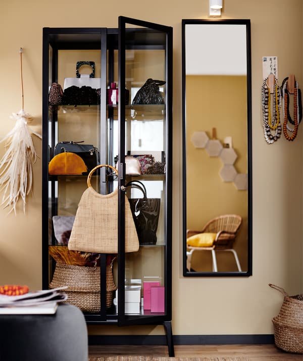 Vitrine à la structure noire remplie d'accessoires et de sacs à main, à côté d'un miroir.