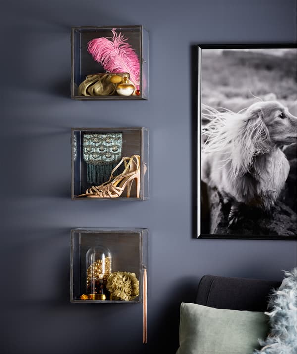 Vitrines BARKHYTTAN exposant une plume rose, des souliers dorés et d’autres objets variés