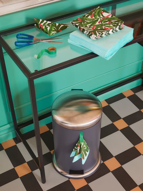 VITTSJÖ stol za laptop postavljen uz zid, gomila FANTASTISK salveta i MJÖSA kanta s pedalom ispod stola.