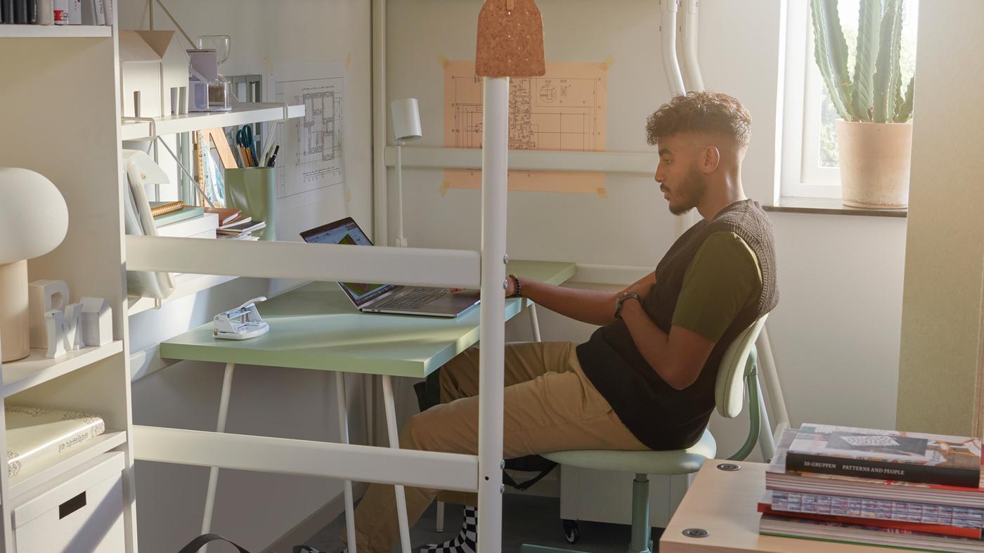 남학생이 VITVAL 비트발 로프트 침대 아래에 있는 LAGKAPTEN 락캅텐 / TILLSLAG 틸슬라그 책상 앞 BLECKBERGET 블레크베리에트 회전의자에 앉아 있는 모습.