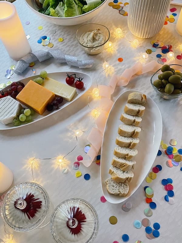 Vogelperspektive auf den gedeckten Tisch. Auf zwei Servierplatten befindet sich jeweils Baguettebrot und eine kleine Käseauswahl.