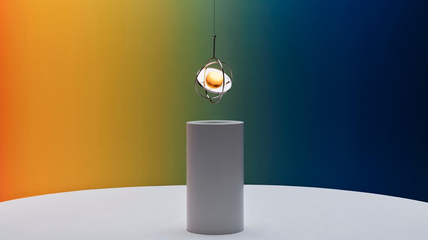 Vor einem Hintergrund in Regenbogenmuster hängt eine SAMMANLÄNKAD LED-Solarleuchte über einem weißen Sockel. 