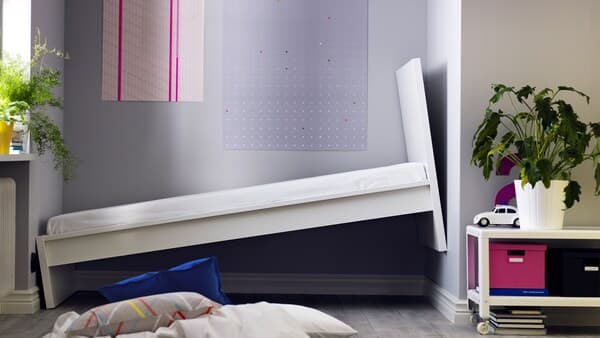 Vor einer bunten Wand steht ein weißes Bett schränk an die Wand angelehnt.