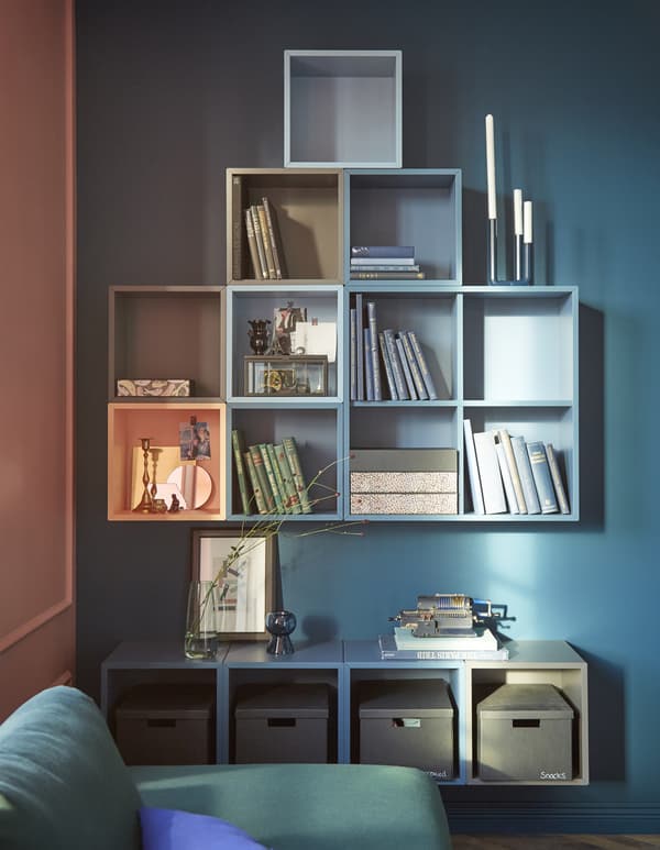 Vous pouvez créer des rangements muraux 100% personnels grâce aux éléments EKET de chez IKEA. Cette combinaison mélange des éléments bleus et gris, avec une touche d’orange pour éclairer le tout.  Les éléments sont regroupés en deux blocs séparés par un large espace, pour créer une zone d’exposition et une table d’appoint.