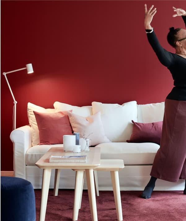 Vrouw staat in een elegante danspose voor een zitbank. Bijpassende meubels, wand, vloerkleed en details in wit en rood.