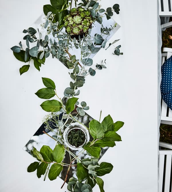 Vue aérienne d’une table avec nappe blanche et chemin de table constitué de miroirs, verdure et petites succulentes