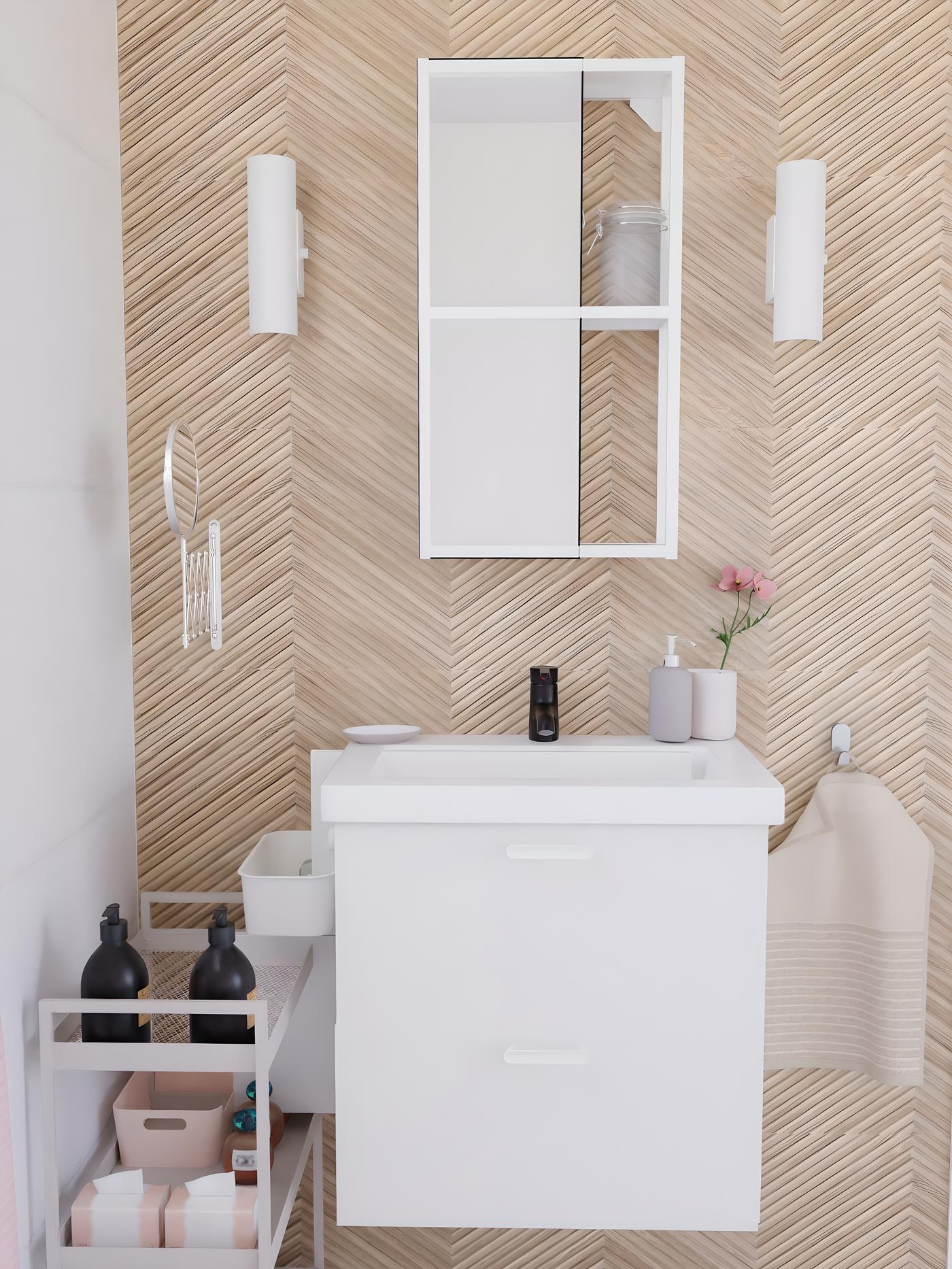 vue de biais d'une salle de bain blanche, dans une suite parentale, avec du linge de bain rose et beige, un mur de carrelage imitation chevron bois clair, et une baignoire blanche