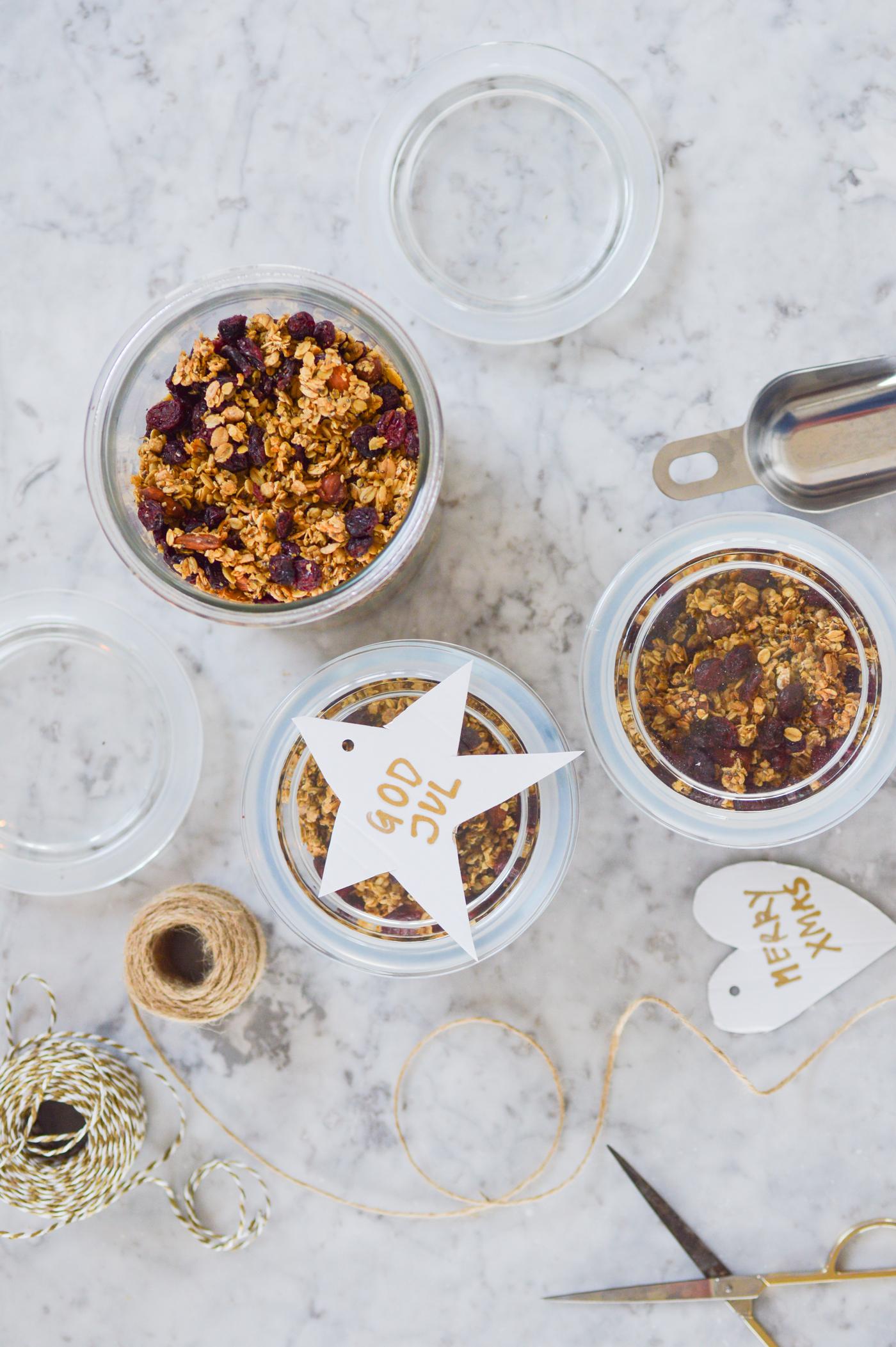 Vue de dessus sur des bocaux remplis de muesli posés sur une surface en marbre, entourés de ficelle, de ciseaux et d'étiquettes cadeaux. Il en résulte une atmosphère festive qui rappelle les cadeaux faits maison.