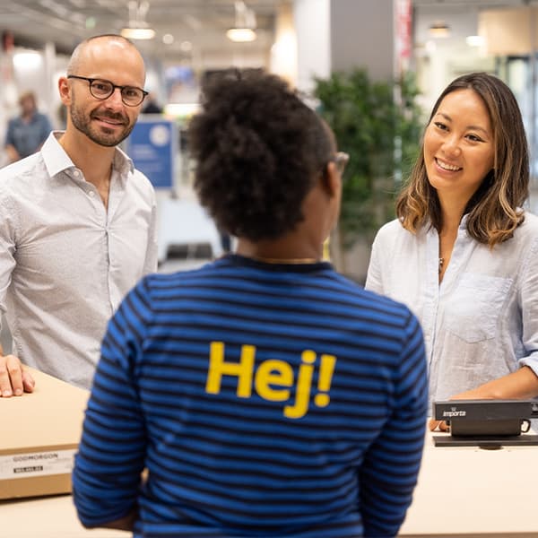 Vue de dos d’un collaborateur IKEA qui accueille deux clients. Les clients sourient.
