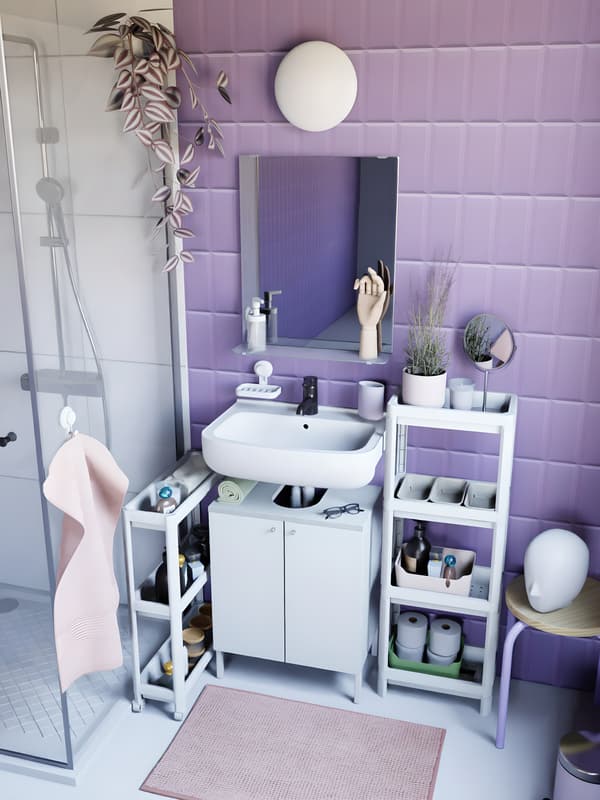 vue de haut d'une salle de bain au carrelage mauve, avec une douche, des meubles blancs, des accessoires mauves et du linge de bain rose. 