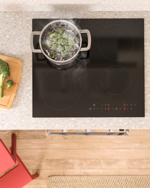 Vue d’en haut d’une table de cuisson à induction noire MATMÄSSIG, avec une casserole où cuisent des brocolis.