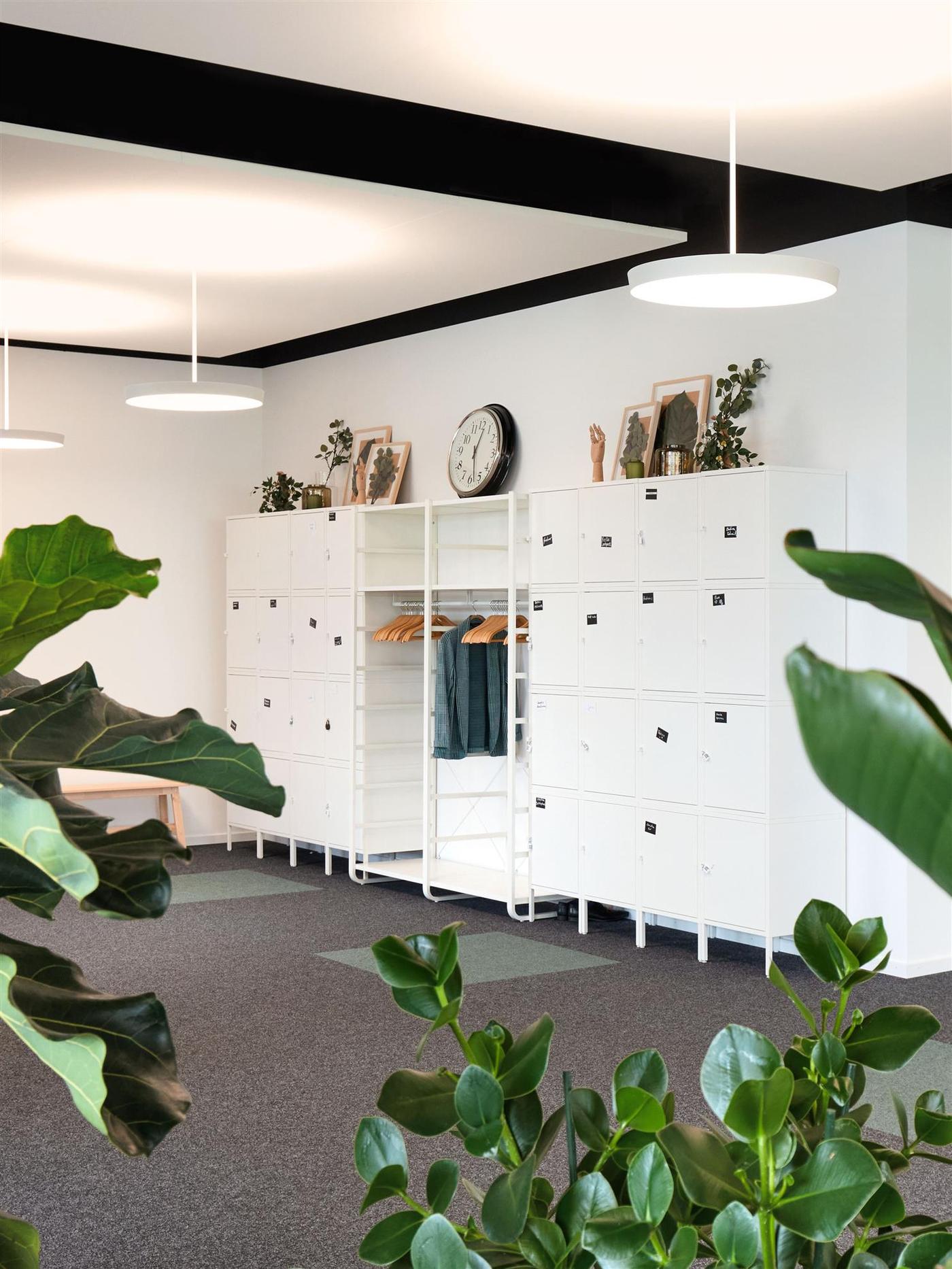 Vue d’un mur dans un bureau avec des casiers et une tringle à vêtements pour y accrocher les vestes des collaborateur-trice-s