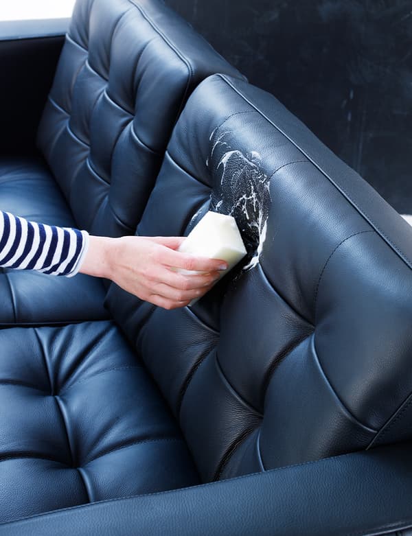 Vue d’une main appliquant un produit d’entretien pour le cuir sur un canapé en cuir noir.